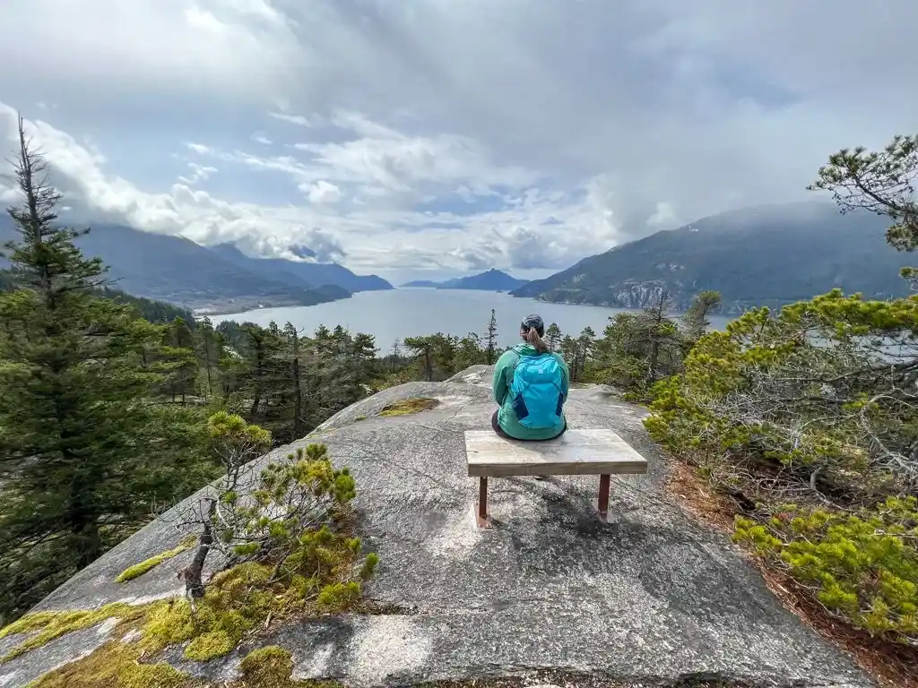 A woman sits on a bench at the viewpoint at Murrin Provincial Park