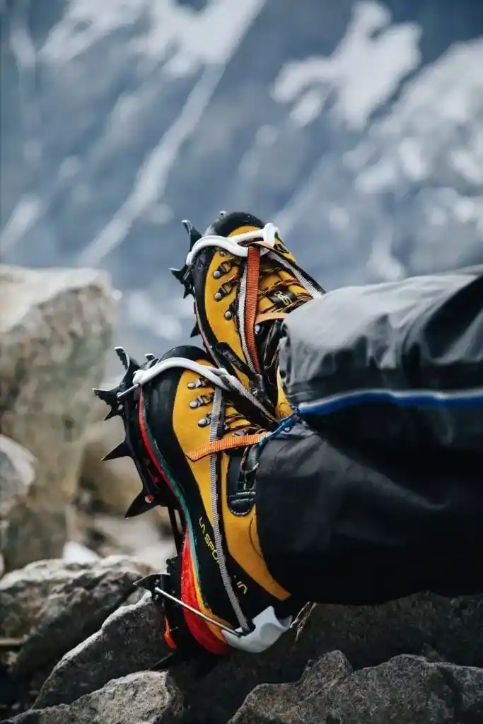 A close up of a pair of mountaineering boots with crampons in front of rocks and snow