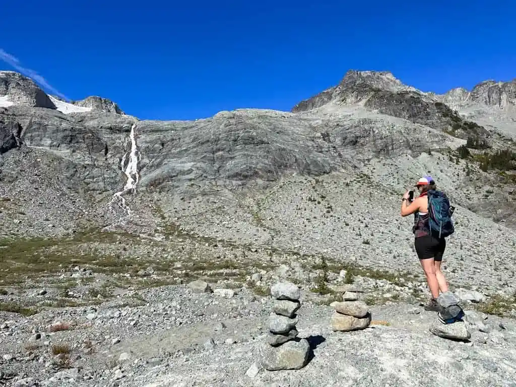 A hiker takes a photo of a waterfall dropping down over a rocky cliff