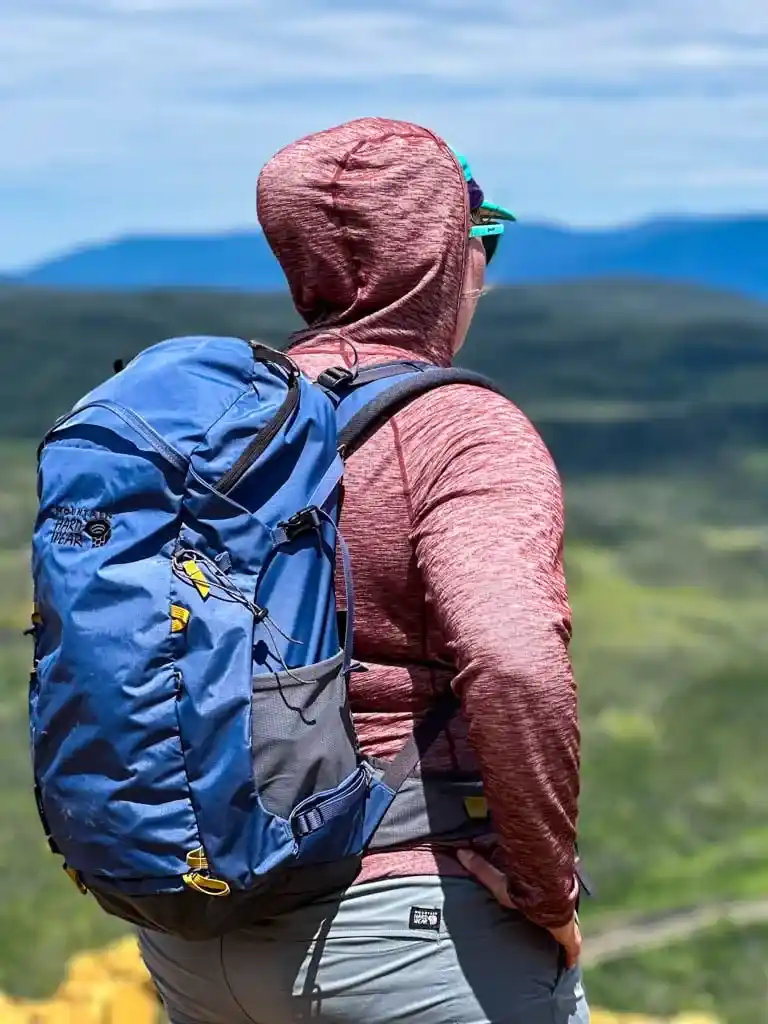 A hiker faces away from the camera. They are wearing the Outdoor Vitals Tern Ultralight Merino Wool Sun Hoodie with the hood up